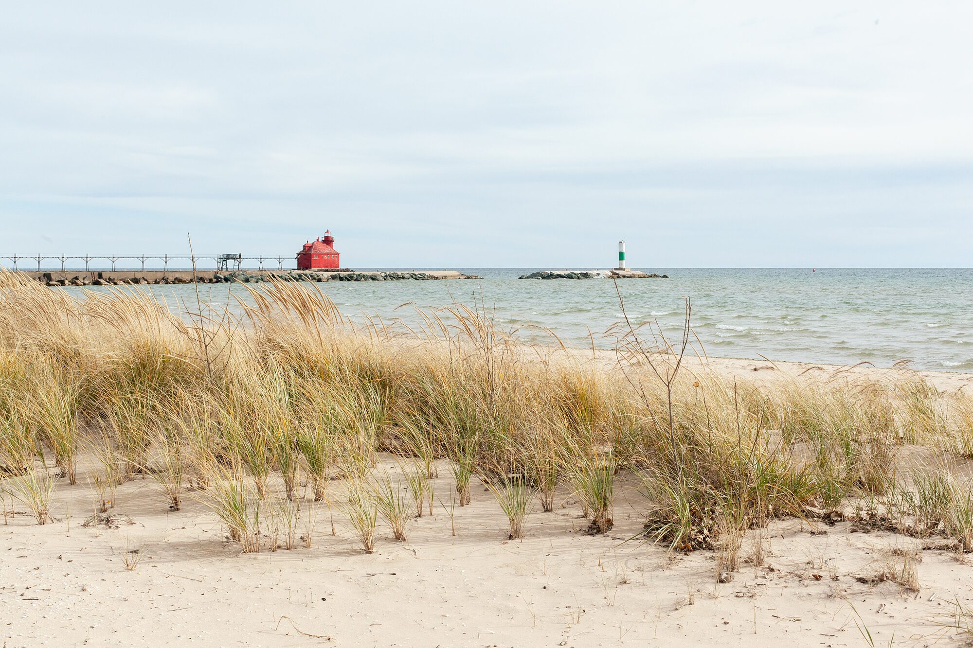 Dune grass on a sandy Lake Michigan shore, looking out to a red lighthouse and pier
