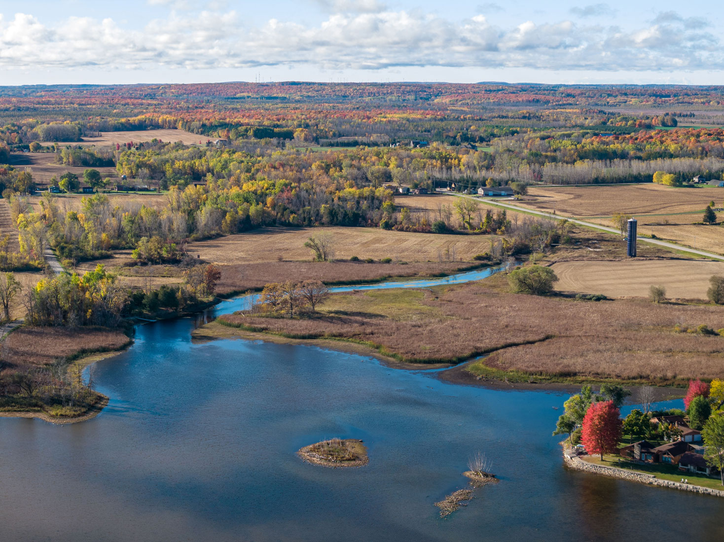 Aerial view of Door County farmland, wetlands, and a winding creek surrounded by fall foliage stretching to the horizon