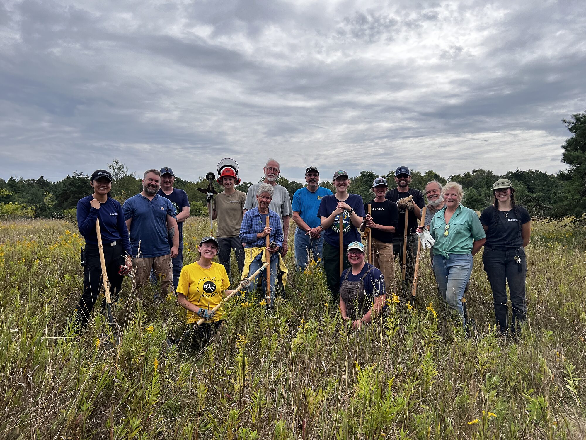 The Stew Crew gathered with their tools in a field after a workday at the Domer-Neff preserve