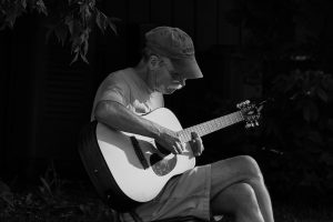 David Warner, a beloved husband and father, sits below a tree strumming his guitar in a moment of serenity