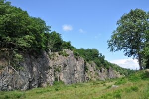 Tall grey bedrock juts out of a grassy area of a forest preserve on the Danish Island of Bornholm. Blue skies illuminate the dramatic scene.