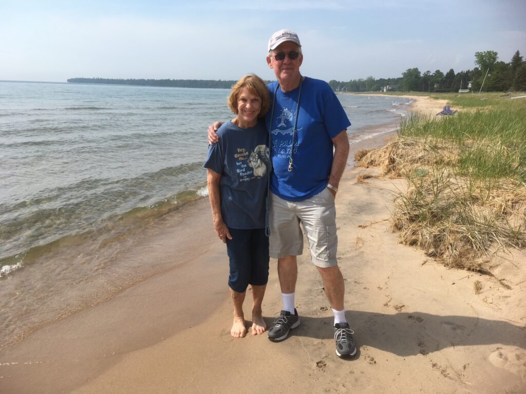 A smiling couple stands on the shores of a sandy beach on a summer day